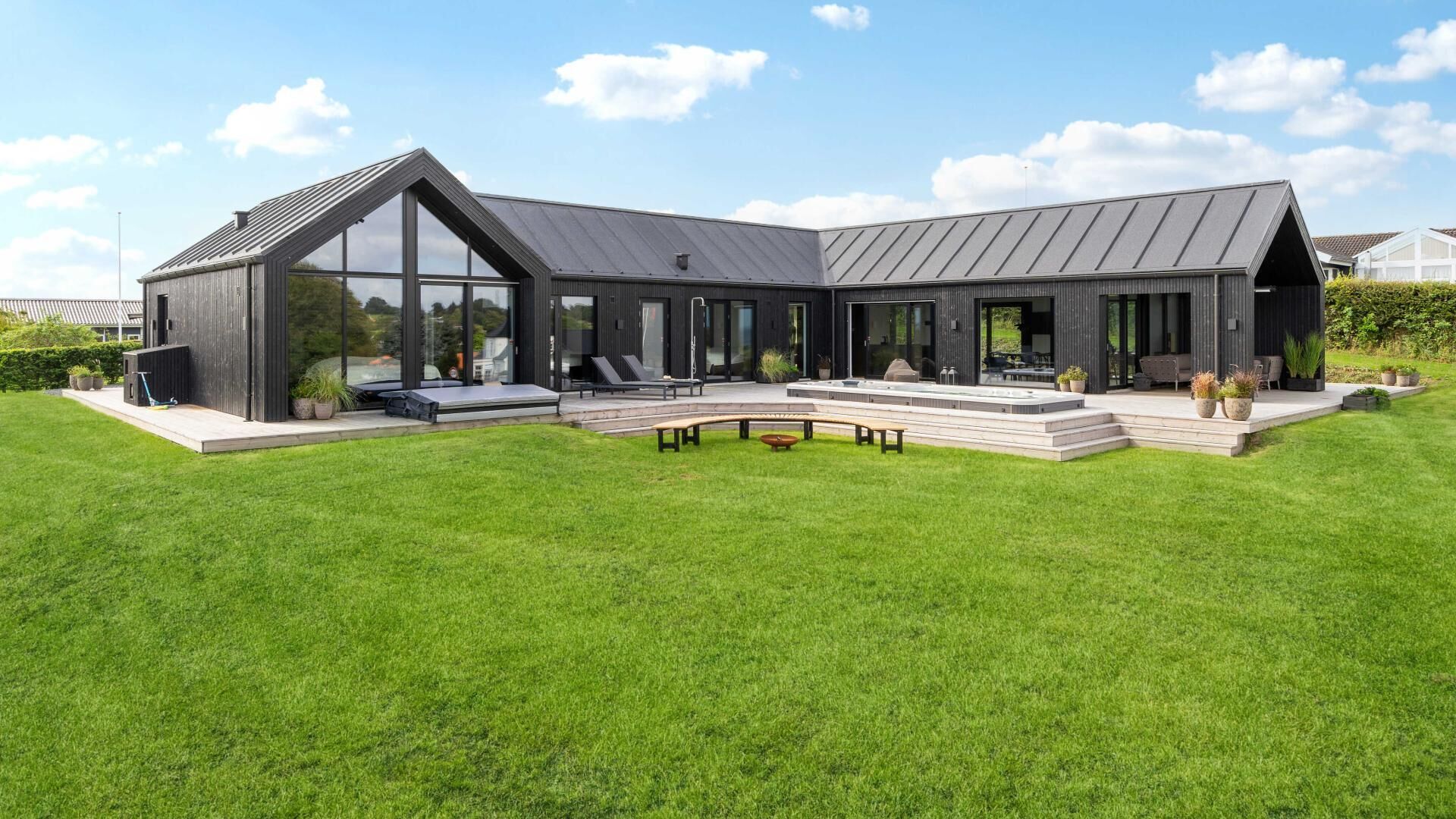 Ein modernes Haus mit großer Glasfassade, überdachter Terrasse und gepflegtem Rasen.