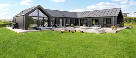 A modern house with a large glass facade, a covered patio, and a well-maintained lawn.