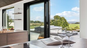 A modern kitchen with a large window, a dining area with a view, and two wine glasses on the table. - VillaVilla 992 - Hejlsminde, Sydjylland (Hejls)