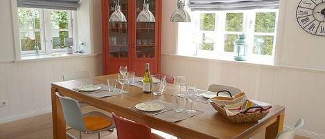A dining area with a wooden table, red and blue chairs, hanging pendant lights, and a red cabinet with glass doors.