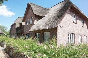 A traditional brick house with a thatched roof and a stone wall in front. - De Gröne Eck 4 House 1 (Nieblum)