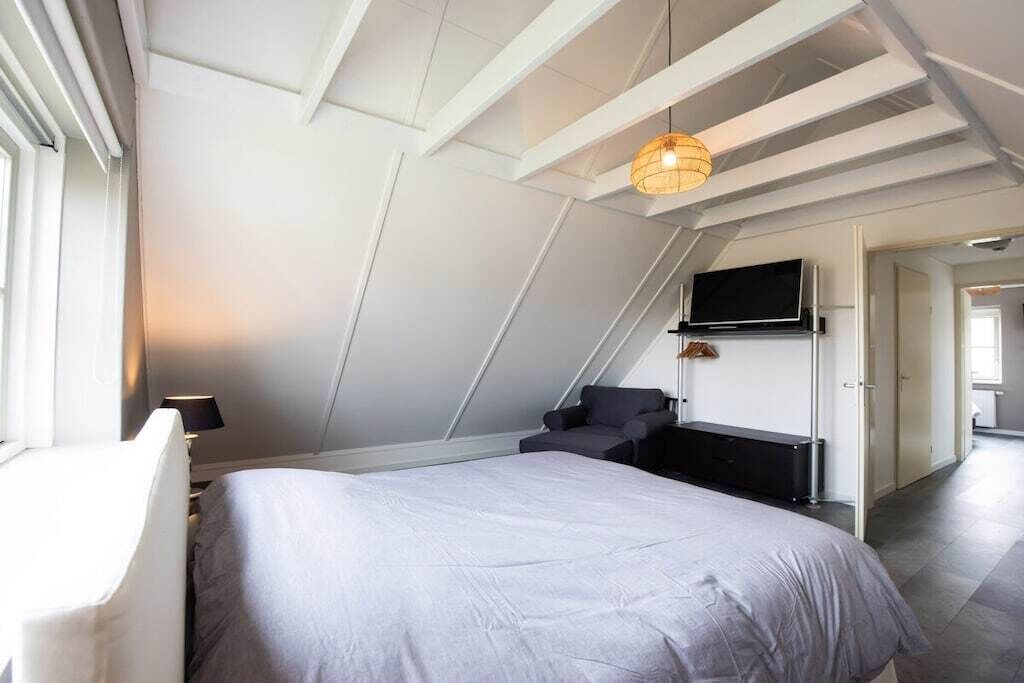 Een moderne slaapkamer met een schuine kap, een bed, een televisie en een werkplek.