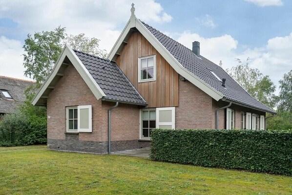 A two-story house with a sloped roof, a brick exterior, and a well-maintained lawn. - Holiday home with 2 bedrooms (Appelscha)