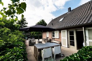 A patio with a table and chairs, a covered area, and a house with a tiled roof and a chimney. - Holiday home with 2 bedrooms (Appelscha)