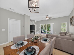 A modern living room with a dining area, a ceiling fan, and a view of the outdoors. - PROMO: 3BR Family Villa with Resort Amenities! - by Blue Sky Villas (Kissimmee)