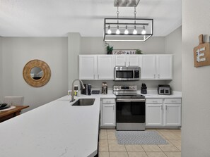 A modern kitchen with white cabinets, a stainless steel microwave, a built-in oven, and a coffee bar sign. - PROMO: 3BR Family Villa with Resort Amenities! - by Blue Sky Villas (Kissimmee)