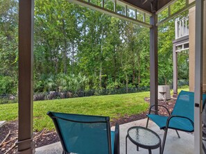 A covered patio with outdoor seating, a view of a landscaped garden, and a building in the background. - PROMO: 3BR Family Villa with Resort Amenities! - by Blue Sky Villas (Kissimmee)