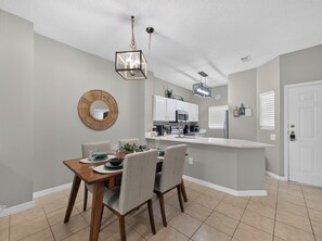 A modern kitchen with white cabinets, a central island, and a dining area with a wooden table and chairs. - PROMO: 3BR Family Villa with Resort Amenities! - by Blue Sky Villas (Kissimmee)