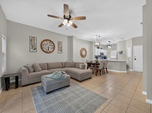 A modern living room with a sectional sofa, a dining table, and a kitchen in the background. - PROMO: 3BR Family Villa with Resort Amenities! - by Blue Sky Villas (Kissimmee)