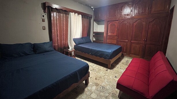 Quarto com duas camas, sofá vermelho, guarda-roupa de madeira e chão em azulejos.