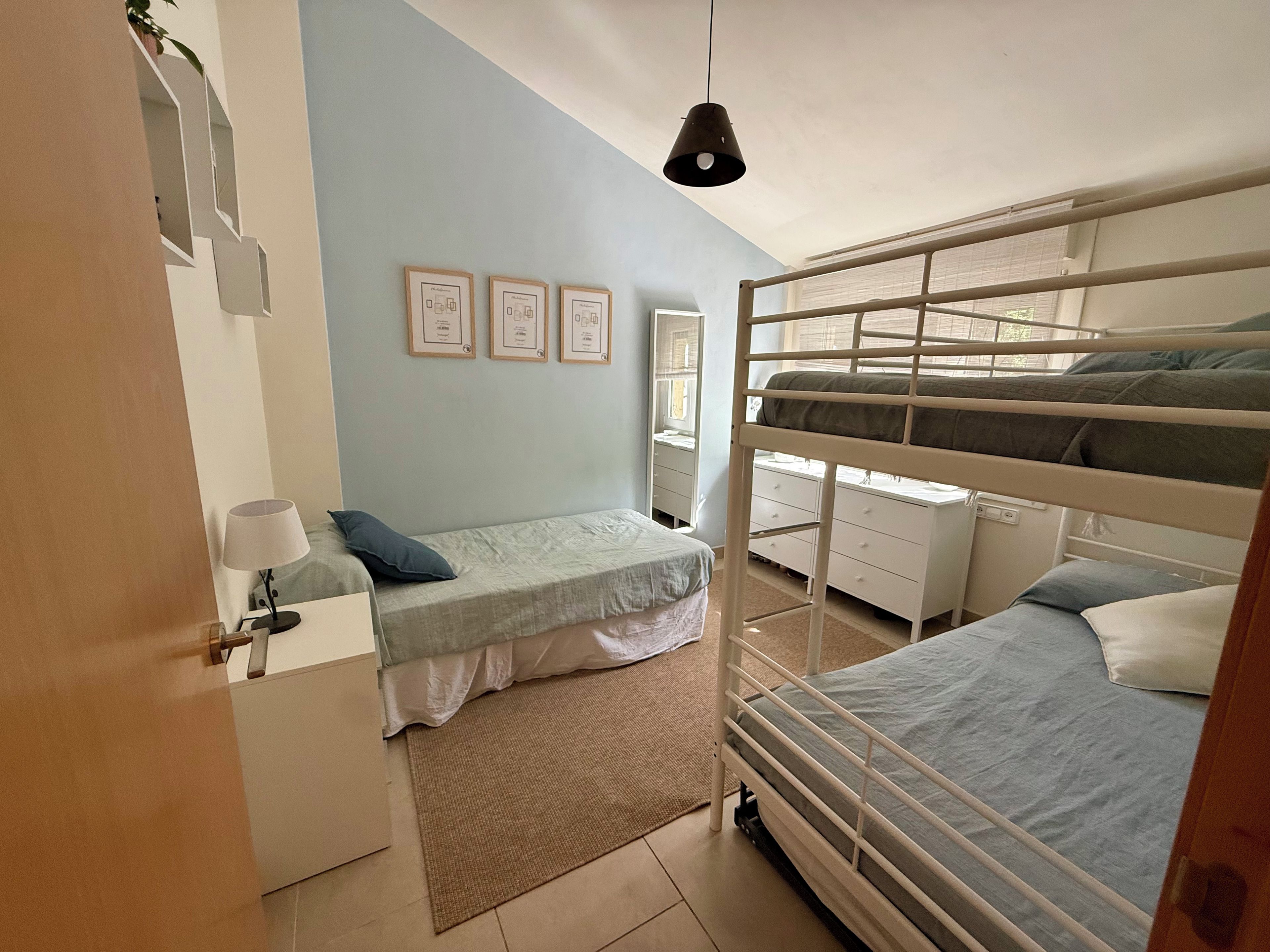 Quarto com beliche, escrivaninha, cadeira, luminária e quadros com certificados na parede.