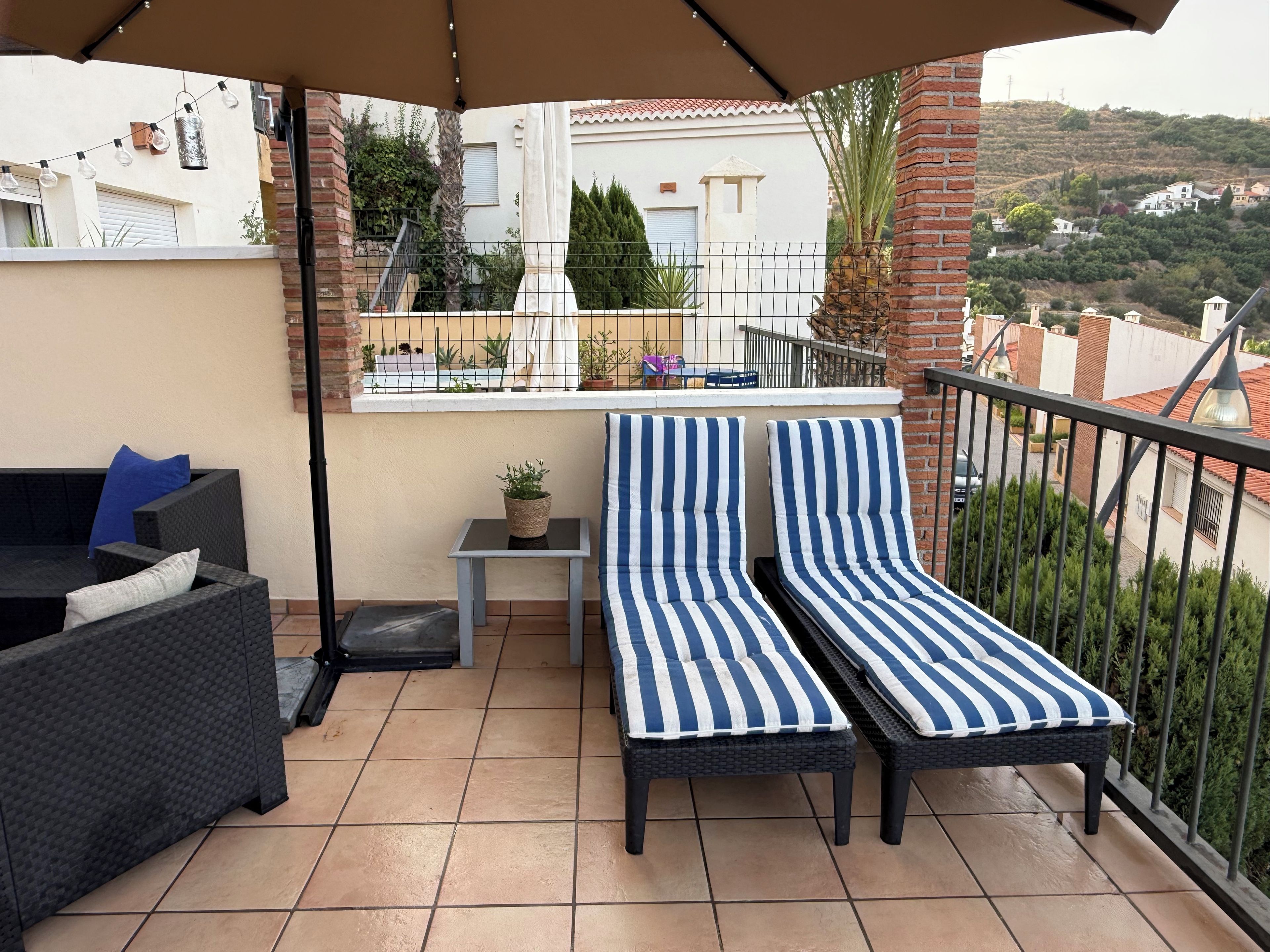 A balcony with two striped lounge chairs, a small table with a plant, and a sofa with cushions.