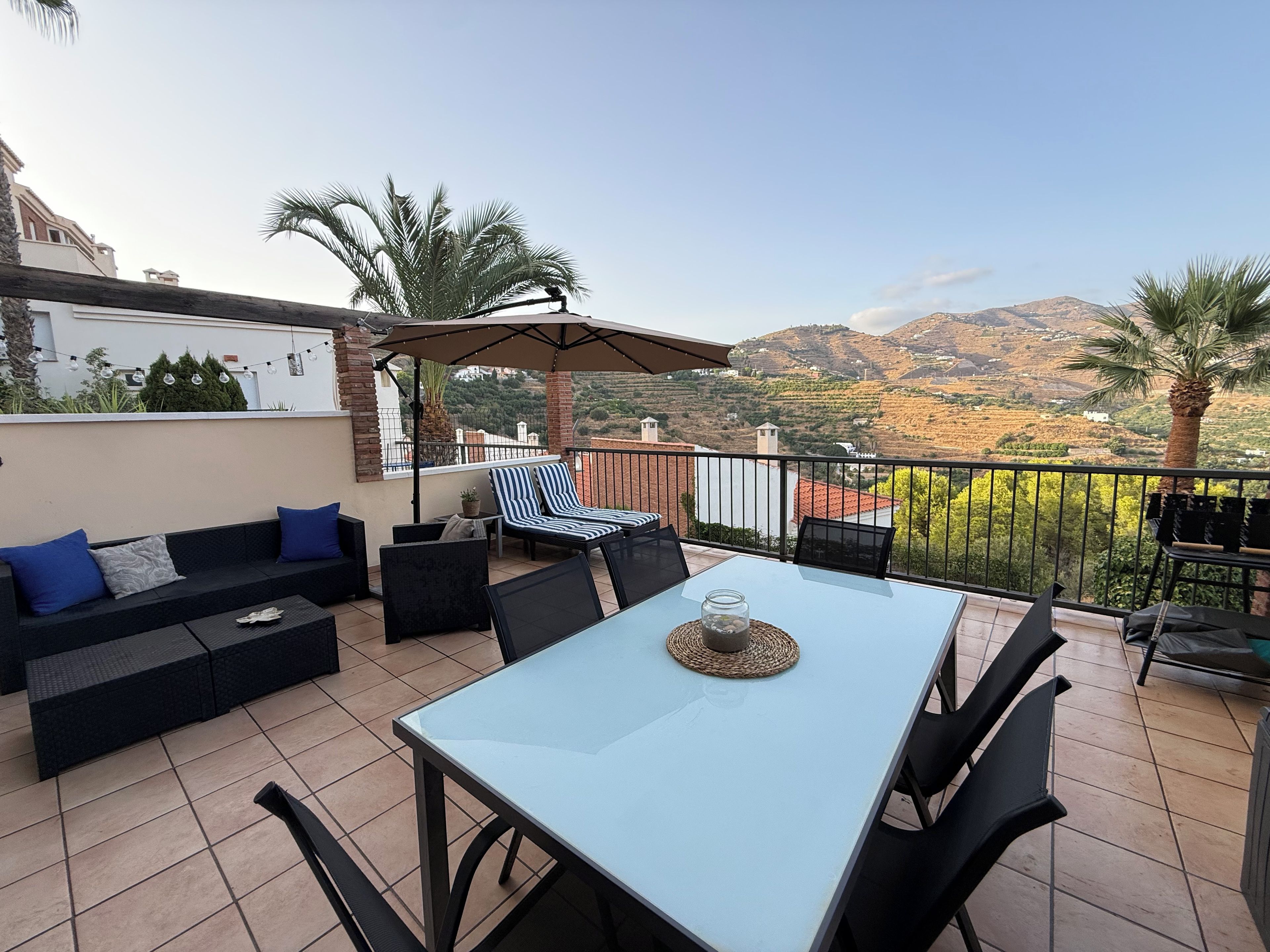 A terrace with a table, chairs, a sofa, and a view of the countryside.