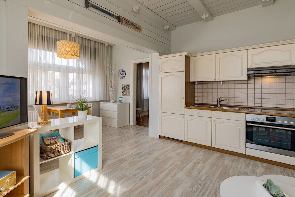 Una cocina moderna con armarios blancos, horno empotrado y ventana con cortinas traslúcidas.