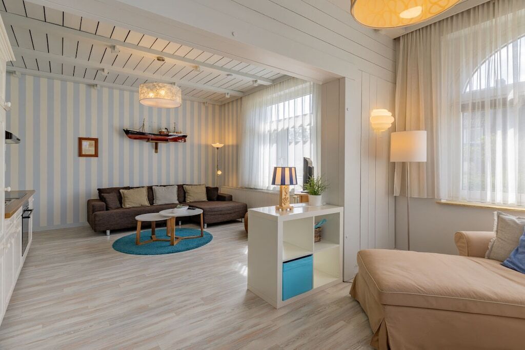 Ein modernes Wohnzimmer mit einer Couch, einem Couchtisch und einem Esstisch. Ein Fenster mit Vorhängen, eine Lampe und ein Regal mit Dekorationen sind ebenfalls vorhanden.
