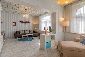 Un salon moderne avec un canapé, une table basse et une table à manger. On y trouve une fenêtre avec des rideaux, une lampe et une étagère ornée d’objets décoratifs.