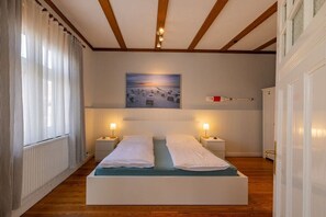 Une chambre à coucher avec un lit, des tables de chevet, un tableau au mur et une fenêtre avec des rideaux.