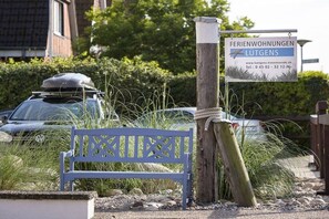 A wooden bench in a garden area with a sign indicating 'FERIENWOHNUNGEN LÜTGENS' and a website address. - Holiday apartment with 1 bedroom (Travemünde)