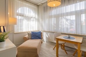 A room with a sofa, a table, and a window with sheer curtains. - Holiday apartment with 1 bedroom (Travemünde)