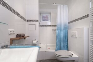A bathroom with a bathtub, toilet, and shower curtain. - Holiday apartment with 1 bedroom (Travemünde)