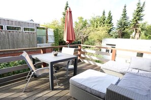 A deck with a table and chairs, a wicker sofa with cushions, and a red umbrella. - Holiday apartment with 1 bedroom (Travemünde)