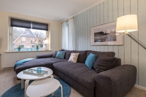 A modern living room with a sectional sofa, a small round table, and a floor lamp. - Holiday apartment with 1 bedroom (Travemünde)