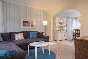 A living room with a sofa, two round tables, a lamp, and a kitchen area in the background. - Holiday apartment with 1 bedroom (Travemünde)