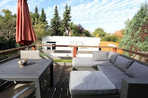 An outdoor deck with a sofa, a table, and an umbrella. - Holiday apartment with 1 bedroom (Travemünde)