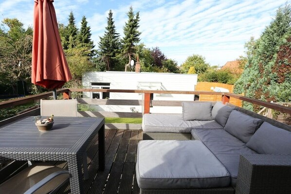 An outdoor deck with a sofa, a table, and an umbrella. - Holiday apartment with 1 bedroom (Travemünde)