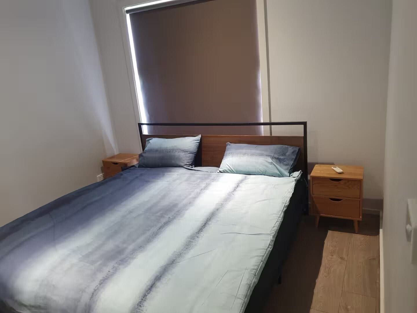 Una cama individual con estructura de madera y dos mesitas de noche, una con cajón y la otra con estante.