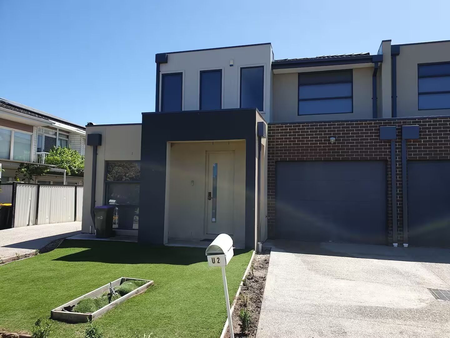 Un edificio residencial moderno con garaje, césped bien cuidado y buzón.