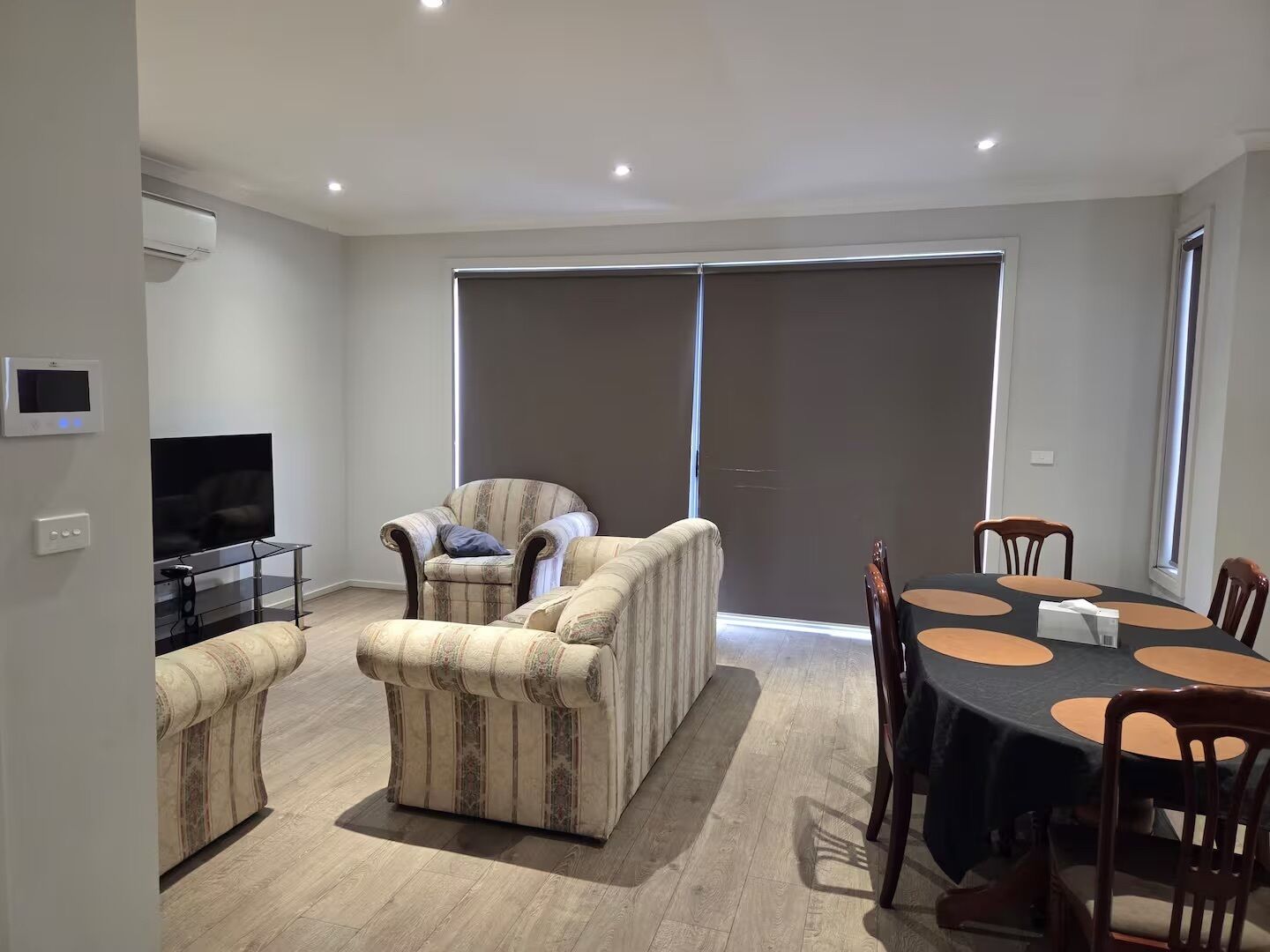 Una sala de estar moderna con sofá, sillones, televisión y un comedor con mesa y sillas.
