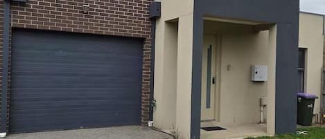 A modern two-story building with a garage, a small porch, and a utility box.