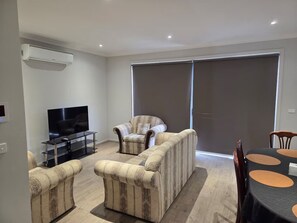 Una sala de estar con una televisión de pantalla plana, un sofá, una silla y una mesa de comedor con mantel negro.