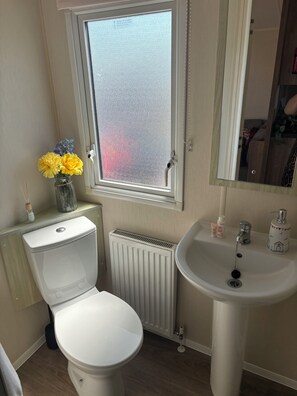 Un baño con inodoro, radiador, lavamanos y ventana con vidrio esmerilado.