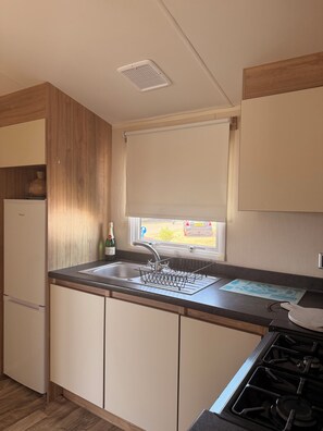 Una kitchenette compacta con un lavamanos integrado, una botella de vino y una ventana con vistas.