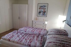 A bedroom with two beds, a white wardrobe, a small bedside table, and a framed picture on the wall. - Holiday apartment with 1 bedroom (Travemünde)