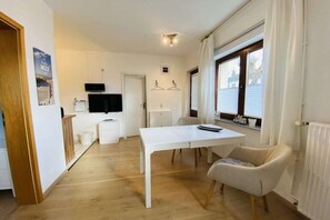 Ein kleiner Wohnraum mit Esstisch, einem Sessel, einem Fernseher und einem Fenster mit Jalousien.