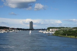 A river with boats, a tall building, and a bridge in the distance. - Holiday apartment with 1 bedroom (Travemünde)