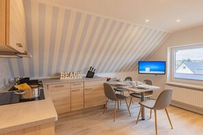 Eine moderne Küche mit Essbereich, einem an der Wand befestigten Fernseher und Blick ins Freie durch ein großes Fenster.