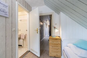A hotel room with a wooden dresser, a bed with a blue pillow, and a bathroom with a towel hanging on the wall. - Holiday apartment with 2 bedrooms (Travemünde)