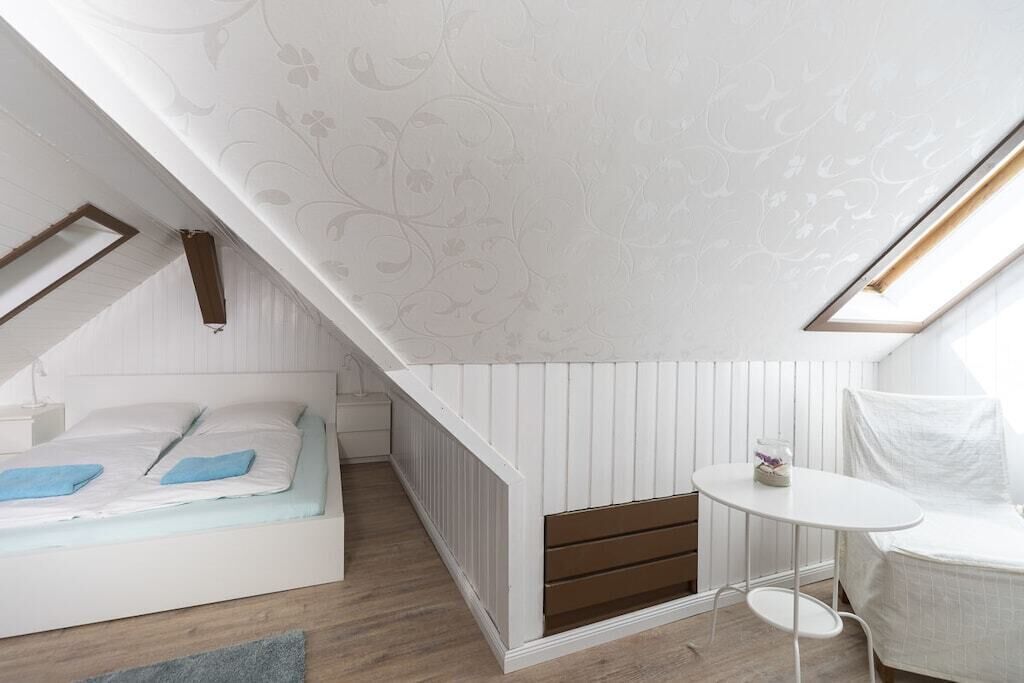 A bedroom with a sloped ceiling, a bed, a small table, and a radiator.