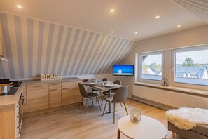 A modern kitchen with a dining area, a flat-screen TV, and a view of the sky through large windows. - Holiday apartment with 2 bedrooms (Travemünde)