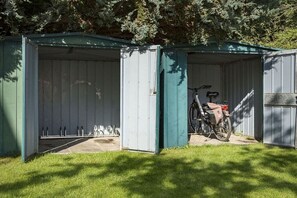 Un cobertizo metálico con la puerta entreabierta, una bicicleta en su interior y un suelo de hormigón.