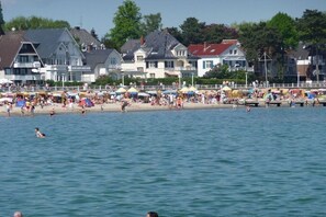A beach with people swimming and sunbathing, houses in the background, and a pier extending into the water. - Holiday apartment with 2 bedrooms (Travemünde)