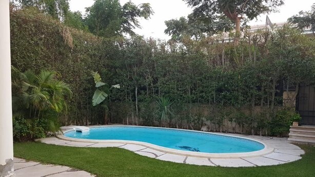 Una piscina con borde de piedra, rodeada por un césped cuidado y abundante vegetación.