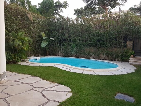 Una piscina con bordo in pietra, circondata da un prato curato e una fitta vegetazione.