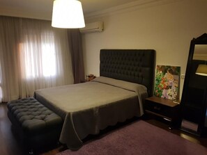 Una camera d'albergo con un letto grande, un comodino, una sedia e un quadro appeso al muro.