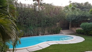 Una piscina de borde curvo, rodeada por un césped cuidado y una valla de madera.