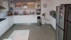Una cocina moderna con armarios blancos, un refrigerador de acero inoxidable y una pequeña mesa blanca con un reloj en la pared.